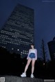 A woman standing in front of a tall building at night.