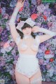 A woman in a white lingerie posing in front of a wall of flowers.