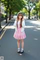 A young woman in a pink dress is standing on the street.