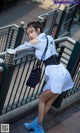 A woman in a white shirt and blue skirt leaning against a railing.