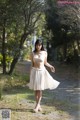 A woman in a white dress is walking down a dirt road.