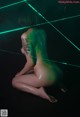 A naked woman sitting on the ground in front of a green light.